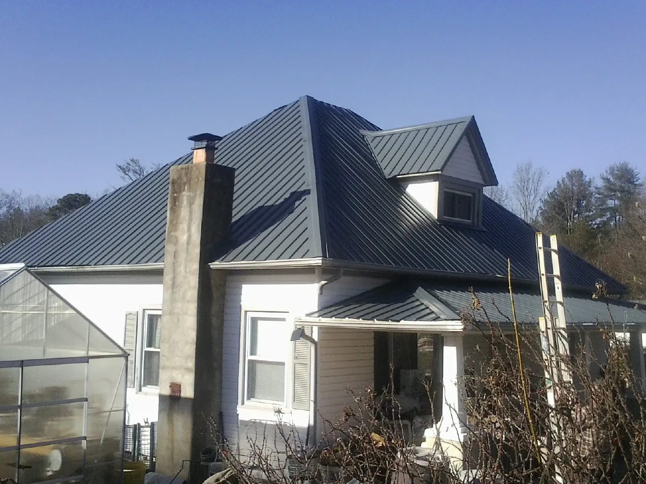 Dark blue standing seam metal roof on a white farmhouse with dormer — Slate & Tile Roof Repair by Roofing Brothers in Excelsior Springs