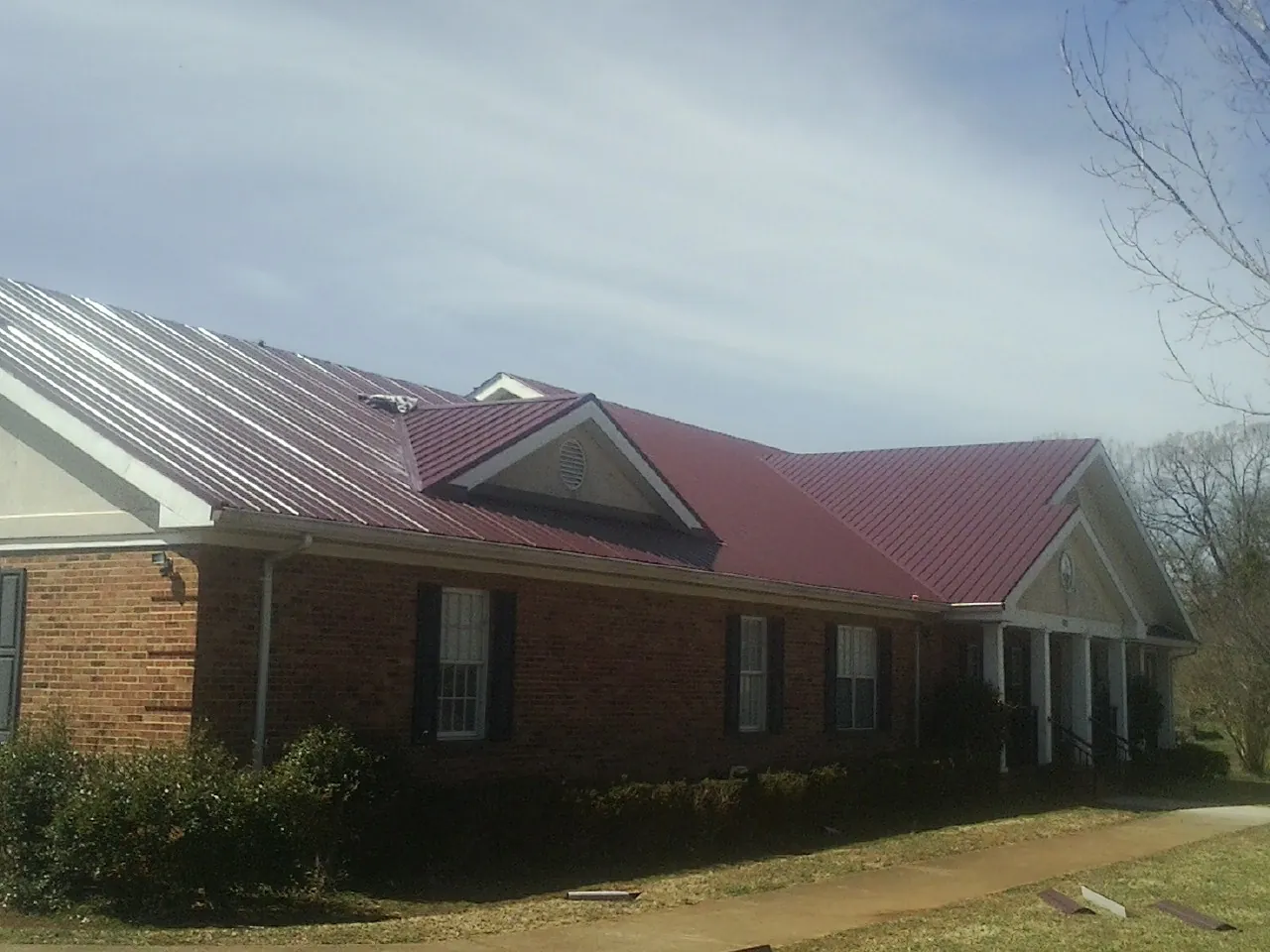 Red metal roof with gabled entries on a long brick building, from a Hail Damage Roof Repair job in Excelsior Springs