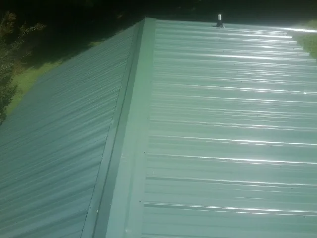 New green metal panels meeting at the ridge of a roof — Flat Roof Repair work by our crew in Excelsior Springs