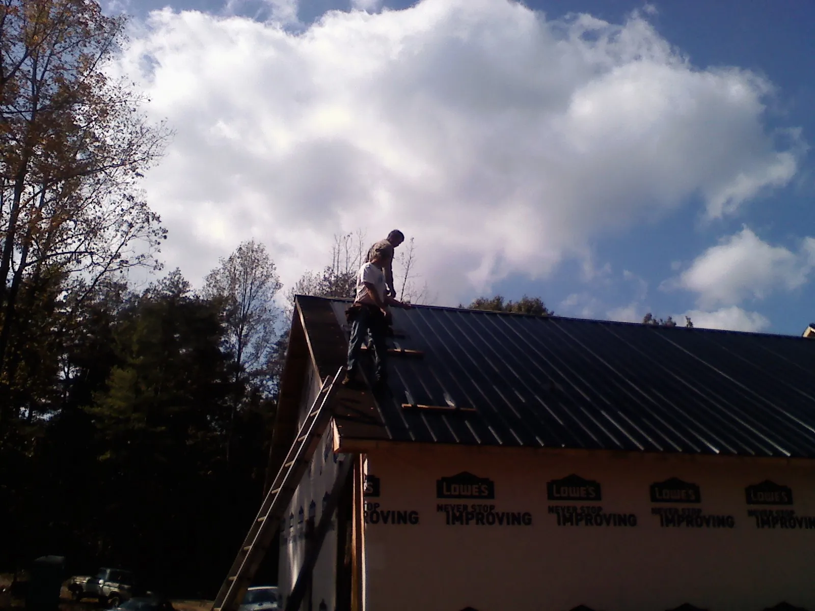 Roofer fastening dark metal panels high against a cloudy sky, from a Roof Inspection job in Excelsior Springs