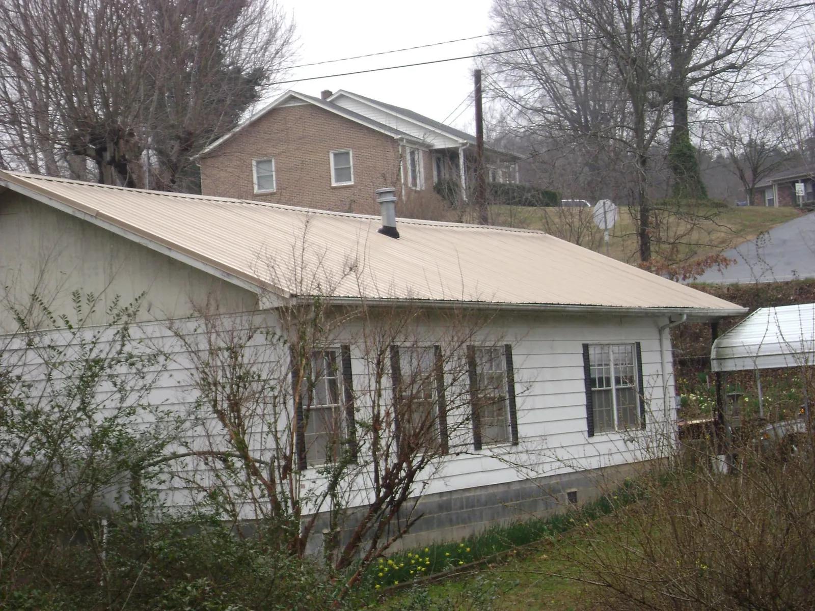 Tan metal roof on a white sided house set into a hillside — Commercial Roofing by Roofing Brothers in Excelsior Springs