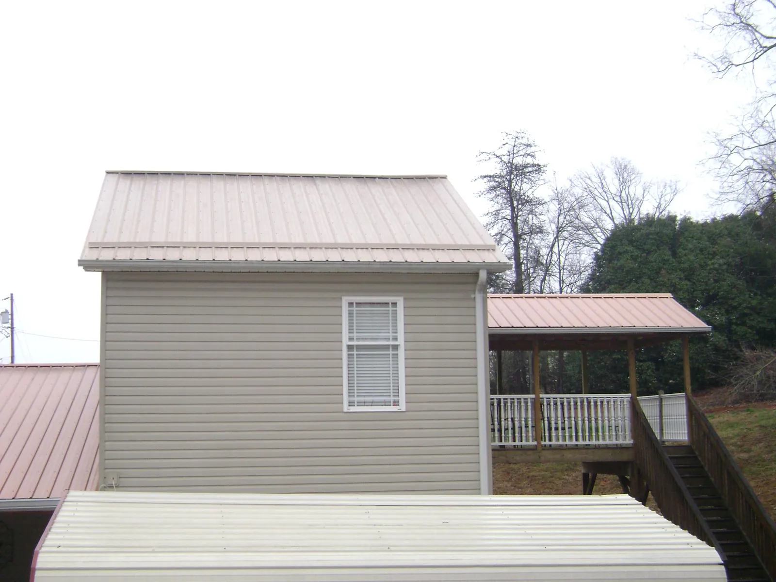 Tan metal roofs on a two story addition and attached porch, from a Roof Replacement job in Excelsior Springs